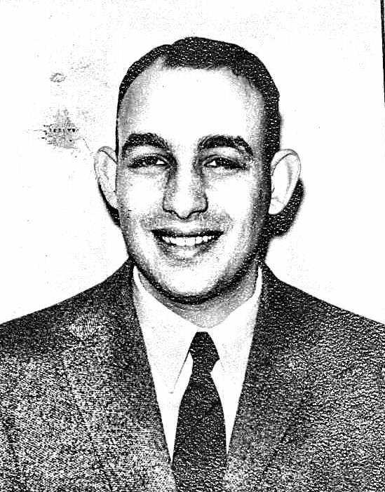 Man with thicker eyebrows smiling wearing coat and tie