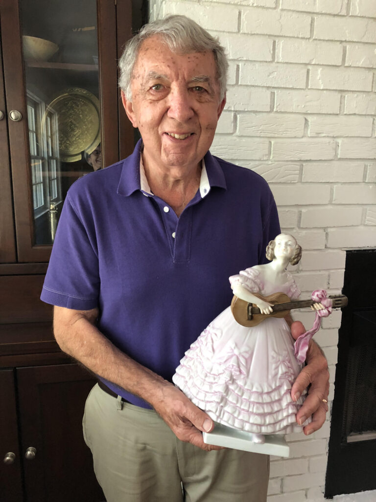 Man holding decorative ceramic doll wearing purple shirt smiling