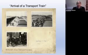 A screenshot of a Zoom presentation showing UAB Professor of History Jonathan Wiesen and a page from a photo album showing three black and white photos under the title "Arrival of a transport train."